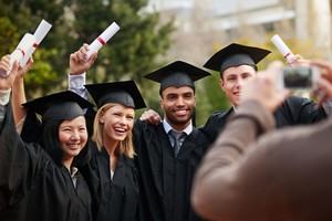 A small group of students celebrate graduating while a friend photographs their celebration