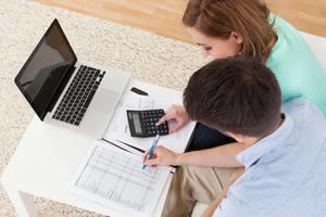 man and woman at desk with laptop, calculator and printed paper with table of numbers