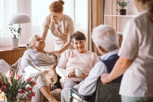 A group of senior citizens in a care home surrounded by care takers.