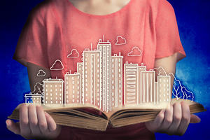 An individual holding a book open with drawings of buildings appearing from the pages. 